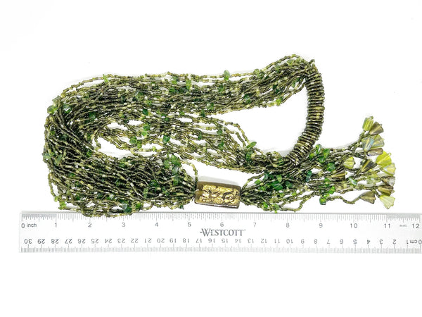 This is a substantial, but easy to wear long 1920s-30s Green Multi Strand Glass Beads Necklace. It made of of thousands of tiny beads in shades of light to deep green. Each bead catches the light and is beautiful. It is anchored by a rectangular green and gold&nbsp; bead which shimmers, introducing a timeless classic in jewelry design.