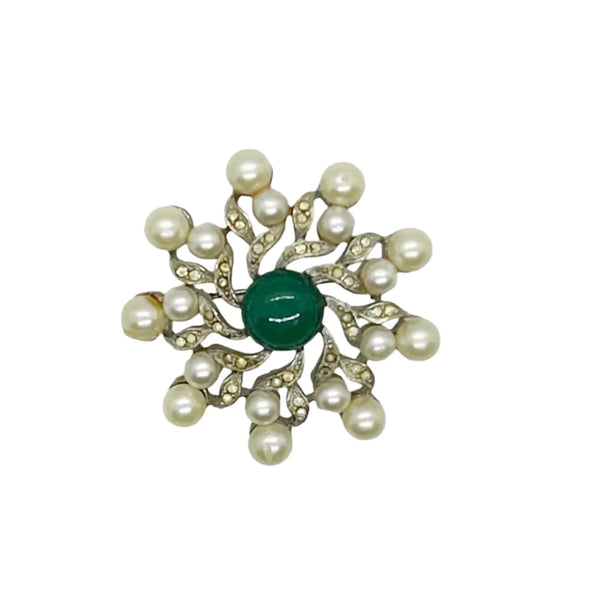  Radiating a regal charm reminiscent of a treasured royal heirloom, it captivates with its intricate design and flawless condition. Measuring 1 3/4" wide, the brooch features a striking green round cabochon centerpiece surrounded by elegant swirling patterns. Cream faux pearls add a soft, classic touch, all set in a lustrous silver-tone metal that enhances its vintage appeal.