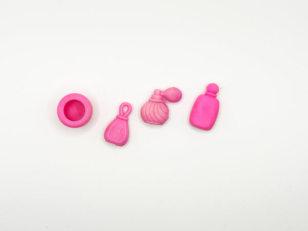 Four small pink molded accessories arranged on a plain white background, including a round cup-like piece, a tassel-shaped piece, a shell-shaped piece with a small round top, and a bottle-shaped piece.
