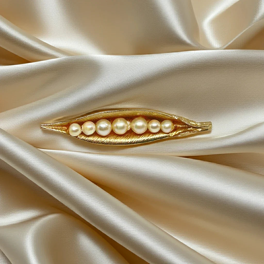 This vintage-inspired brooch features a brushed gold finish and showcases seven delicately graduated faux pearls, measuring 2.75 inches in length.