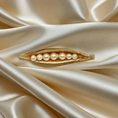 This vintage-inspired brooch features a brushed gold finish and showcases seven delicately graduated faux pearls, measuring 2.75 inches in length.