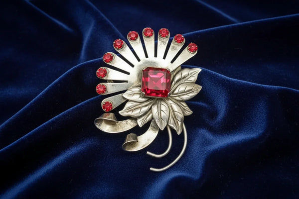 This opulent, abstract floral vintage brooch was made by Brookcraft, and is made of detailed leaves with bright red stones and a large diamond shaped center stone. The stones are open backed and the large stone is prong set. Brookcraft was in business from the 1930s until 1952. They were renowned for their fine, handmade pieces and use of Sterling Silver