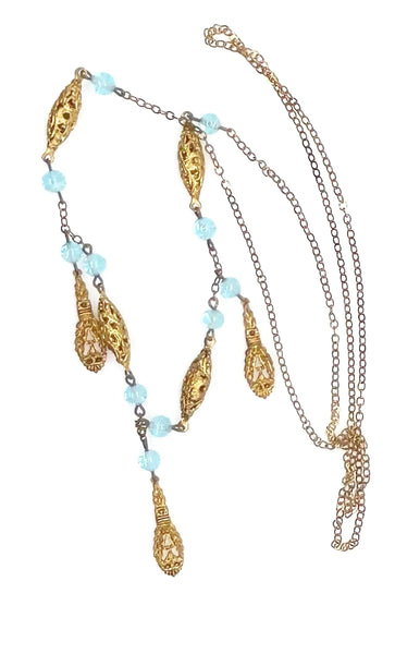 This is a beautiful antique drop necklace, made of golden filigree beads interspersed with clear blue glass accent beads, and punctuated by flat abstract filigree drops. 