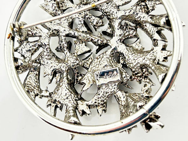 This striking, rounded, and very detailed brooch pendant makes a beautiful necklace. It measures 2" across and comes on a 24" chain with a secure fold-over clasp. The pendant features a strong, eye-catching frame that showcases a delicate floral motif, complete with blooms and leaves