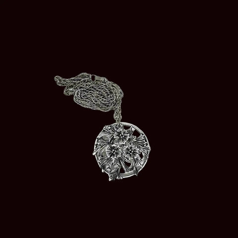 This striking, rounded, and very detailed brooch pendant makes a beautiful necklace. It measures 2" across and comes on a 24" chain with a secure fold-over clasp. The pendant features a strong, eye-catching frame that showcases a delicate floral motif, complete with blooms and leaves