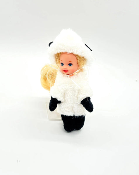 A front view of a vintage 4-inch Mattel Barbie Kelly Club Melody doll dressed as a little lamb. The miniature doll has blonde hair, blue eyes, and wears a white plush fleece lamb costume complete with a hood featuring black ears, a yellow bow under the chin, and black paw details on the hands and feet. Isolated on a crisp white background