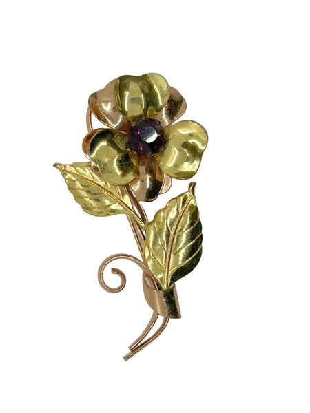 Gold flower-shaped brooch with a purple gemstone on a white background