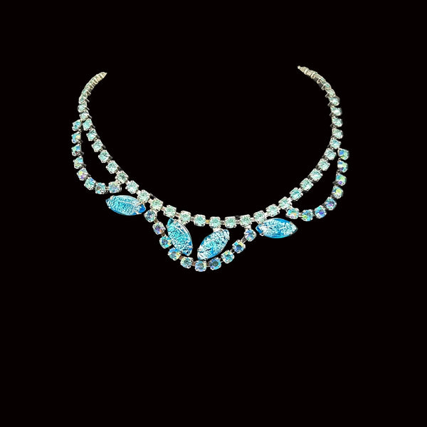 This stunning vintage necklace features a simple chain of medium blue rhinestones. The centerpiece is truly captivating, with three elements—each made of a strand of blue rhinestones—draping over marquise-shaped, iridescent blue confetti lucite. 