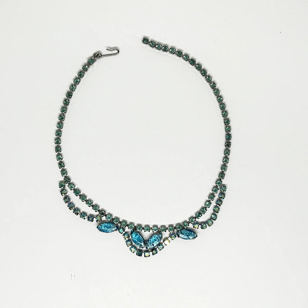 This exquisite brooch with an Old World aesthetic showcases finely crafted gold filigree petals encircling a square stone in elegant blue-purple tones. Between each delicate petal rests a round, iridescent stone that complements the central hues, adding subtle depth and shimmer.