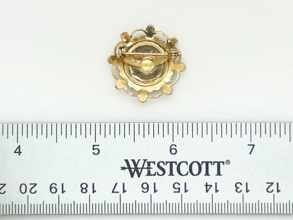Take a look at this vintage costume jewelry brooch featuring a hand-painted pink rose on a white enamel or ceramic base, set within an ornate gold-tone filigree frame accented with pink rhinestones. The center showcases a pink rose, with green dots accenting the perimeter. The setting and metalwork around the outside are particularly lovely. It measures 1" across.