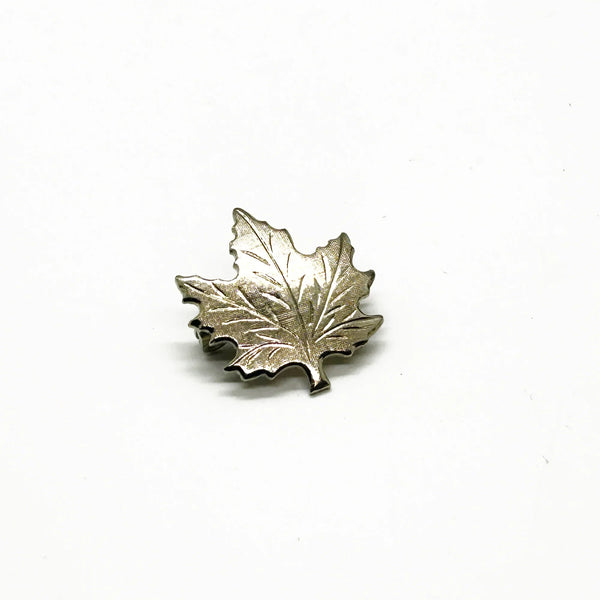 Add a touch of vintage charm to your wardrobe with this delightful silver maple leaf pin! This little beauty- measuring just 1" across- showcases intricate etching that brings the iconic leaf to life, complete with a textured finish that catches the light beautifully.