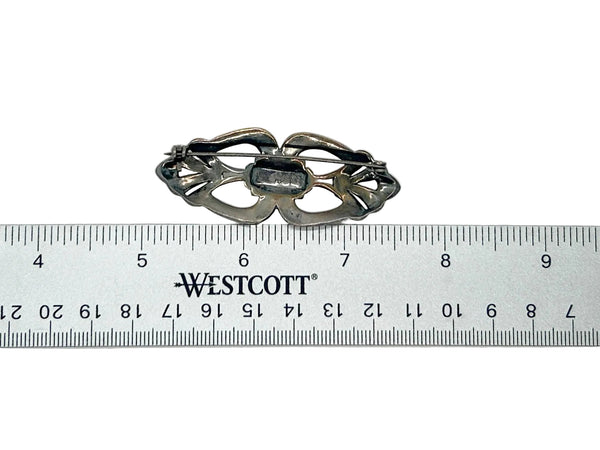 Symmetrical Art Deco silver brooch with geometric openwork loops and central marcasite stone inlay.