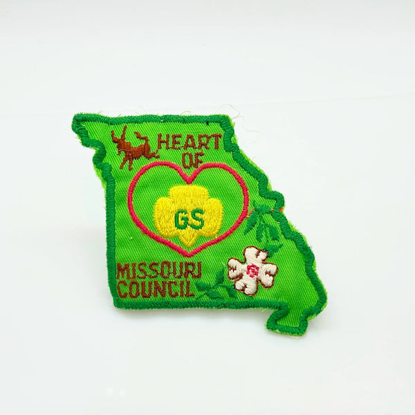 This authentic vintage shoulder patch celebrates the Heart of Missouri Girl Scout Council, once based in Jefferson City and Columbia. The distinctive Missouri-shaped design features a prominent pink heart showcasing the iconic Girl Scout "GS" logo at its center. 