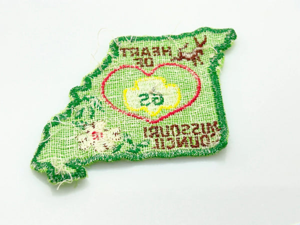 This authentic vintage shoulder patch celebrates the Heart of Missouri Girl Scout Council, once based in Jefferson City and Columbia. The distinctive Missouri-shaped design features a prominent pink heart showcasing the iconic Girl Scout "GS" logo at its center. 