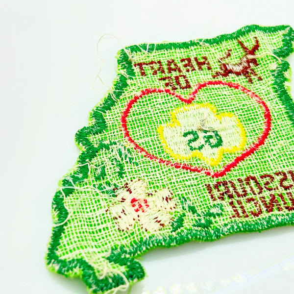 This authentic vintage shoulder patch celebrates the Heart of Missouri Girl Scout Council, once based in Jefferson City and Columbia. The distinctive Missouri-shaped design features a prominent pink heart showcasing the iconic Girl Scout "GS" logo at its center. 