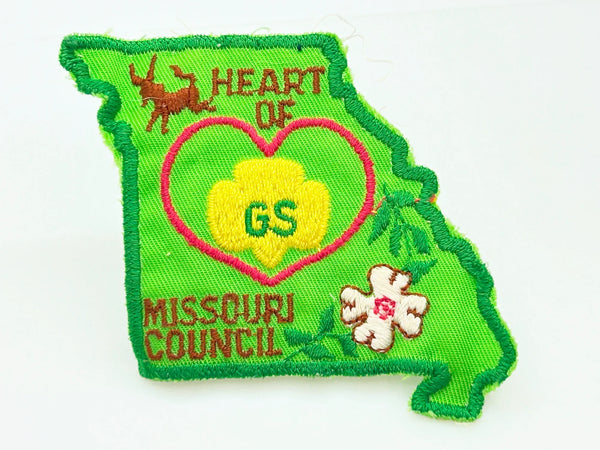 This authentic vintage shoulder patch celebrates the Heart of Missouri Girl Scout Council, once based in Jefferson City and Columbia. The distinctive Missouri-shaped design features a prominent pink heart showcasing the iconic Girl Scout "GS" logo at its center. 