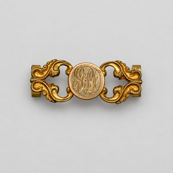 Antique Victorian monogrammed watch slide in gold-tone metal. Features a round hand-engraved monogram center and highly detailed repoussé scrollwork side accents, perfect as a jewelry making component