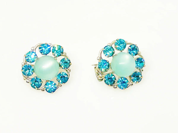 This is a hard-to-find set featuring a brooch, a pair of scatter pins, and screw-back earrings. The design showcases round, frosted light turquoise cabochons. Each features a center moonglow stone surrounded by bright, faceted, slightly deeper blue stones, all prong-set. 