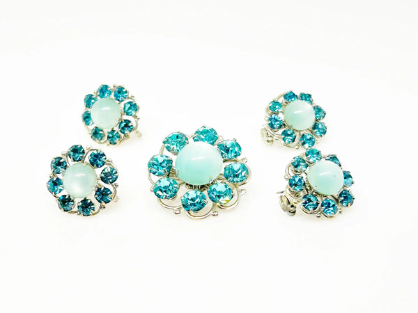 This is a hard-to-find set featuring a brooch, a pair of scatter pins, and screw-back earrings. The design showcases round, frosted light turquoise cabochons. Each features a center moonglow stone surrounded by bright, faceted, slightly deeper blue stones, all prong-set. 