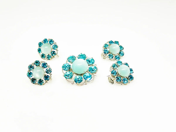 This is a hard-to-find set featuring a brooch, a pair of scatter pins, and screw-back earrings. The design showcases round, frosted light turquoise cabochons. Each features a center moonglow stone surrounded by bright, faceted, slightly deeper blue stones, all prong-set. 