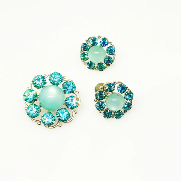 This is a hard-to-find set featuring a brooch, a pair of scatter pins, and screw-back earrings. The design showcases round, frosted light turquoise cabochons. Each features a center moonglow stone surrounded by bright, faceted, slightly deeper blue stones, all prong-set. 