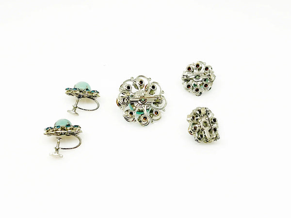 This is a hard-to-find set featuring a brooch, a pair of scatter pins, and screw-back earrings. The design showcases round, frosted light turquoise cabochons. Each features a center moonglow stone surrounded by bright, faceted, slightly deeper blue stones, all prong-set. 