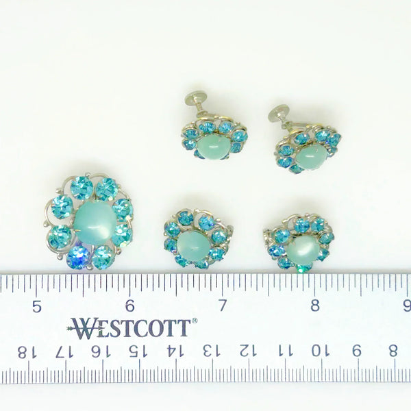 This is a hard-to-find set featuring a brooch, a pair of scatter pins, and screw-back earrings. The design showcases round, frosted light turquoise cabochons. Each features a center moonglow stone surrounded by bright, faceted, slightly deeper blue stones, all prong-set. 