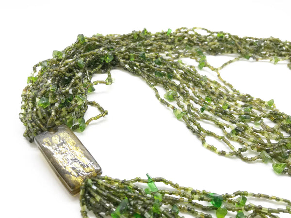 This is a substantial, but easy to wear long 1920s-30s Green Multi Strand Glass Beads Necklace. It made of of thousands of tiny beads in shades of light to deep green. Each bead catches the light and is beautiful. It is anchored by a rectangular bead which shimmers. Introducing a timeless classic in jewelry design.