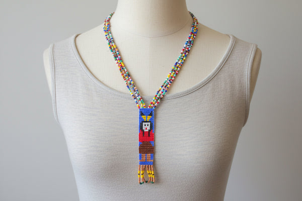 This is a striking example of vintage Native American-style hand-beaded necklace, featuring a loom-woven pendant of a female figure. These necklaces are handcrafted using colorful glass seed beads and often include traditional design elements such as looped fringe detail. These pieces are generally created using a flat, loom-woven technique