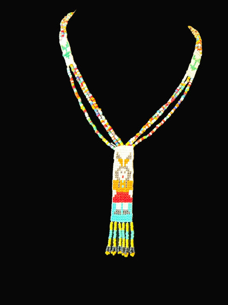 This striking Native American beaded necklace features a beautifully detailed figure adorned with two feathers in flowing black hair, dressed in a brown tunic and red skirt with black shoes. The design showcases a white upper background that transitions to a vibrant turquoise-teal green below, creating visual depth and interest. 