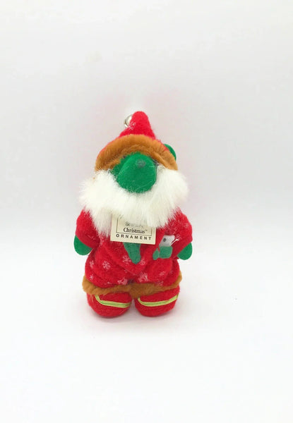 A small plush Christmas gnome ornament wearing a red outfit with green accents, a white beard, and a brown hat.