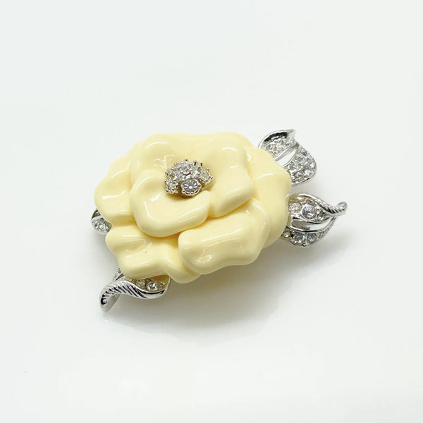 Vintage Nolan Miller Lara camellia flower brooch featuring carved cream lucite petals, a central clear rhinestone cluster, and textured silver-tone metal leaves
