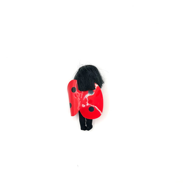 Rear view of a miniature ladybug character doll with black hair and a red-and-black spotted shell costume for a product listing image
