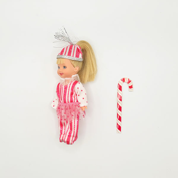 Vintage 2001 Mattel Barbie Kelly Club doll, Kelly as Peppermint Girl from the Barbie in the Nutcracker collection, shown standing next to her striped candy cane accessory on a white backdrop