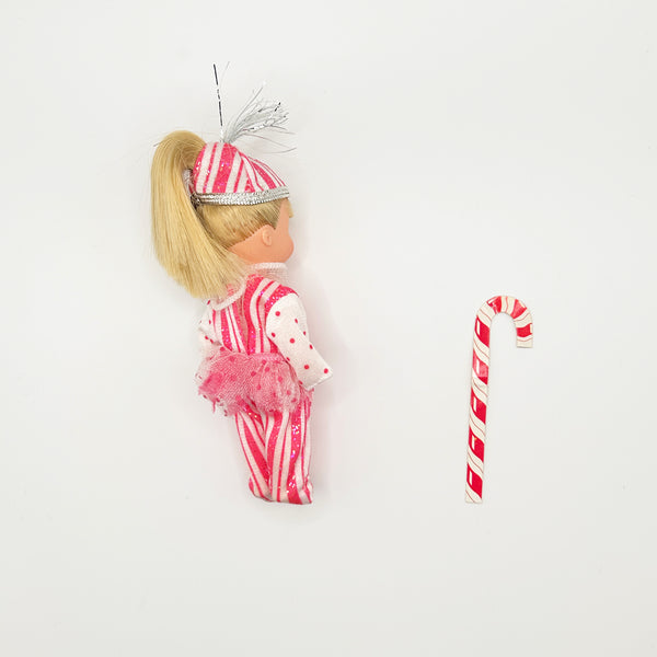 Back view of vintage 2001 Barbie Kelly as Peppermint Girl doll with blonde ponytail, striped hat with silver tinsel, and pink tutu, shown alongside her candy cane accessory
