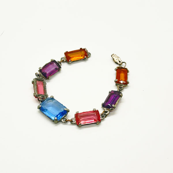 A vintage-style bracelet featuring multiple rectangular, baguette-cut gemstones in vibrant colors including blue, pink, red, orange, and purple, set in an antique gold-tone metal.