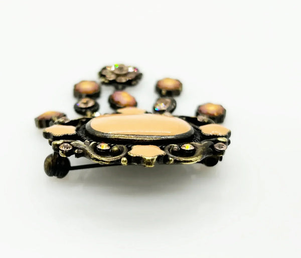 Level up your vintage jewelry collection with this stunning coral-hued brooch that captures timeless elegance. The piece showcases a luminous pale melon-orange centerstone framed by delicate star-shaped accents and peachy rhinestones that catch the light beautifully.