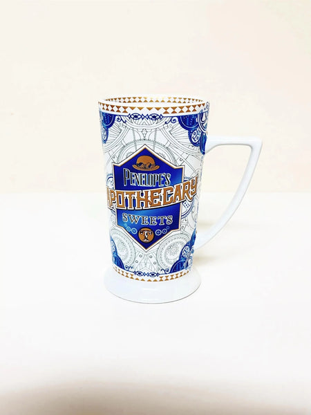 Universal Studios Toothsome Chocolate Emporium Penelope's Apothecary Sweets tall ceramic pedestal mug with blue, white, and gold geometric pattern on a solid white background.