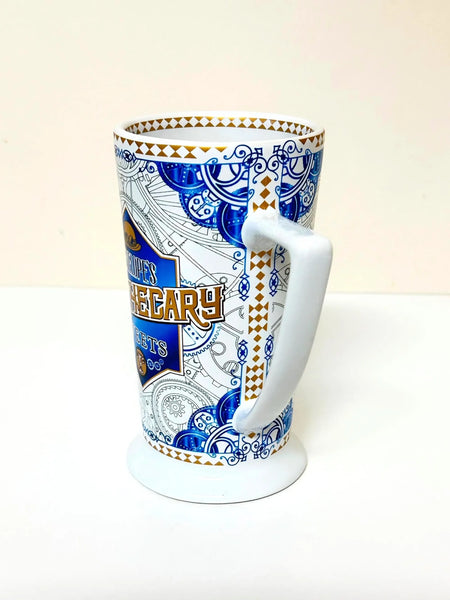 Universal Studios Toothsome Chocolate Emporium Penelope's Apothecary Sweets tall ceramic pedestal mug with blue, white, and gold geometric pattern on a solid white background.