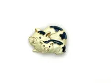 A vintage DKI gold-tone enamel brooch shaped like two snuggling black and white spotted pigs on a white background.