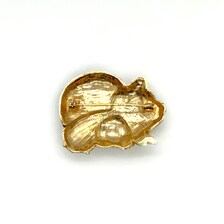 A vintage DKI gold-tone enamel brooch shaped like two snuggling black and white spotted pigs on a white background.