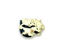 A vintage DKI gold-tone enamel brooch shaped like two snuggling black and white spotted pigs on a white background.