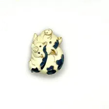A vintage DKI gold-tone enamel brooch shaped like two snuggling black and white spotted pigs on a white background.