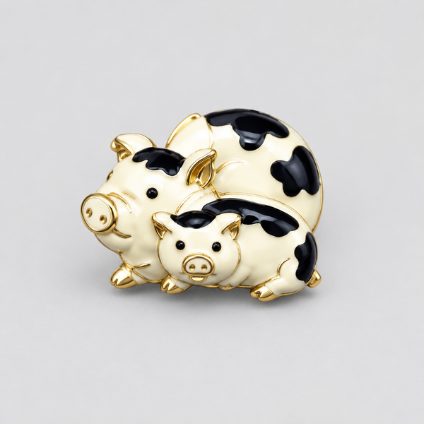 A whimsical vintage gold-tone brooch featuring a stacked pair of cream enamel pigs decorated with smooth black cow-print spots. The playful design highlights polished gold-plated snouts, ears, and hooves, cleanly photographed against a neutral light gray background.