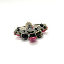 Vintage costume jewelry brooch pin featuring a central rhinestone cluster encircled by a halo of clear crystals, with alternating pear-cut pink faux rubies and round faceted gunmetal black stones in a dark metallic prong setting.