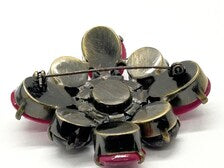 Vintage costume jewelry brooch pin featuring a central rhinestone cluster encircled by a halo of clear crystals, with alternating pear-cut pink faux rubies and round faceted gunmetal black stones in a dark metallic prong setting.