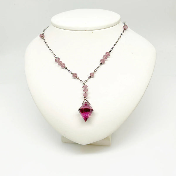 This stunning vintage crystal necklace showcases clusters of deep purple bicone beads, interspersed with sleek paper clip chains. It culminates in a magnificent faceted diamond-shaped stone. Measuring 16.5 inches in length, with a drop of 1.5 inches from the center, this piece exudes elegance and sophistication.