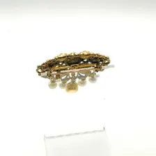 Product photo of a vintage antique-gold filigree pin. The central oval frame holds bright green and red glass gems. Six small dangling charms hang from the bottom, including five creamy white pearls and one round green rhinestone.