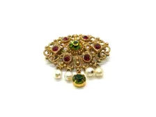 Product photo of a vintage antique-gold filigree pin. The central oval frame holds bright green and red glass gems. Six small dangling charms hang from the bottom, including five creamy white pearls and one round green rhinestone.