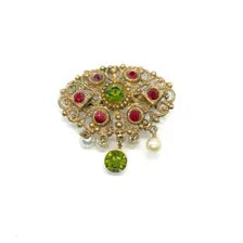 Product photo of a vintage antique-gold filigree pin. The central oval frame holds bright green and red glass gems. Six small dangling charms hang from the bottom, including five creamy white pearls and one round green rhinestone.